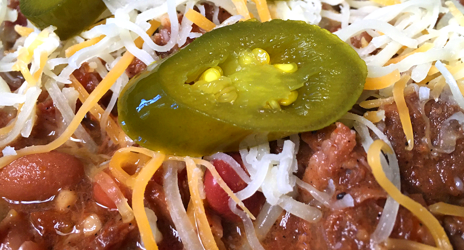 a close-up of a sliced jalapeno sitting on top of chili and cheese